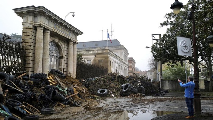Gedung Pemerintah Prancis Dipenuhi Sampah Imbas Protes Petani People watch slurry, manure and tyres dumped by farmers at the entrance of the local state administration building, in Agen, southwestern France, Saturday, Jan. 27, 2024. French farmers have vowed to continue protesting and are maintaining traffic barricades on some of the country's major roads. The government announced a series of measures Friday but the farmers say these do not fully address their demands. (AP Photo/Fred Scheiber)