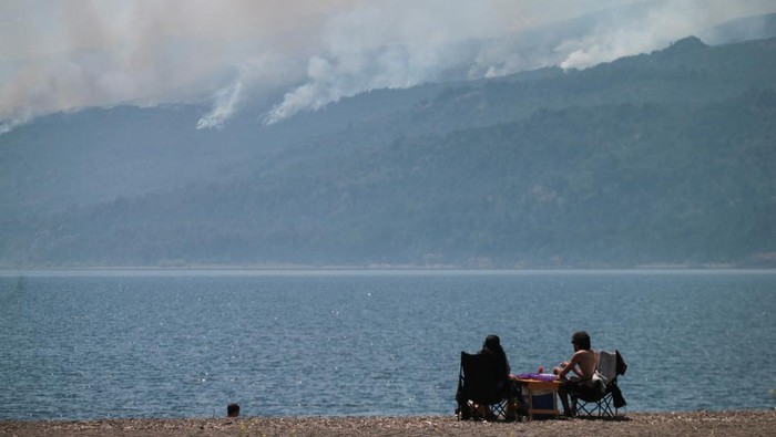 Tourists enjoy the day at the Futalaufquen Lake as smoke rises from trees as a wildfire burns at Los Alerces National Park, in Chubut, Argentina January 28, 2024. REUTERS/Martin Levicoy NO RESALES. NO ARCHIVES