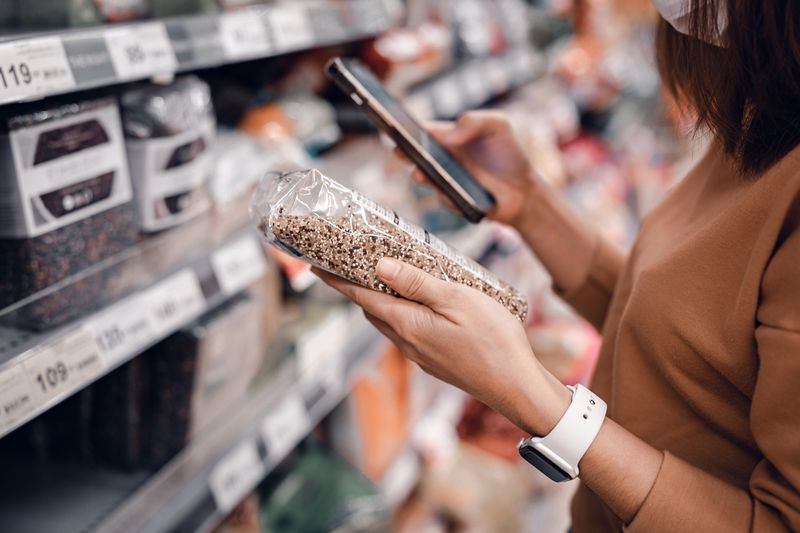 1317610306 Closeup - Woman shopping in supermarket and reading product information. Costumer buying food at the market.