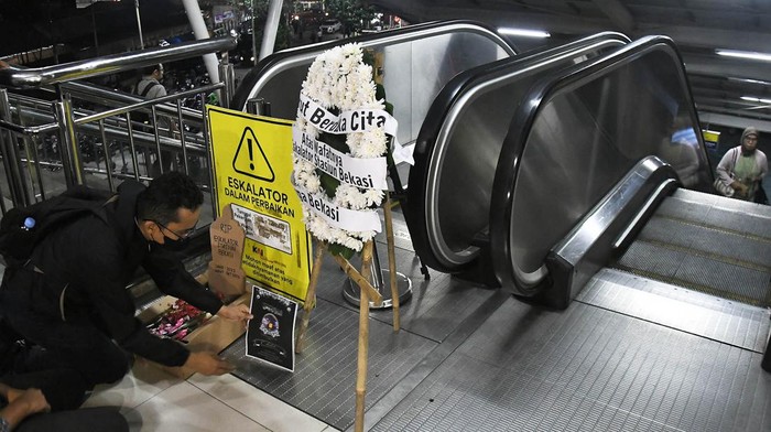Seorang penumpang kereta melakukan aksi dengan membawa bunga bertuliskan ?Turut berduka cita atas wafatnya satu eskalator? di Stasiun Bekasi, Jawa Barat, Rabu (31/1/2024). Aksi tersebut sebagai bentuk kritik penumpang angkutan umum kereta karena sudah 100 hari, satu eskalator di stasiun rusak sehingga menganggu kenyamanan penumpang.