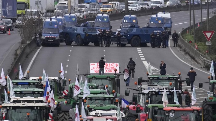 Farmers watch their tractors from a bridge on a blocked highway, Wednesday, Jan. 31, 2024 in Chilly-Mazarin, south of Paris. French farmers maintained their protests on major roads around Paris and across the country on Wednesday as police was deployed to protect the capital, its airports and an international market. (AP Photo/Christophe Ena)