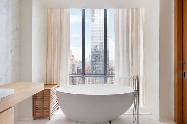 Kamar mandi dilengkapi bathtub yang langsung menghadap ke jendela kaca besar. Meski marmer menjadi material utama, aksen kayu hadir untuk menghadirkan sentuhan yang hangat. (Foto: Dok. Daniel Wang)