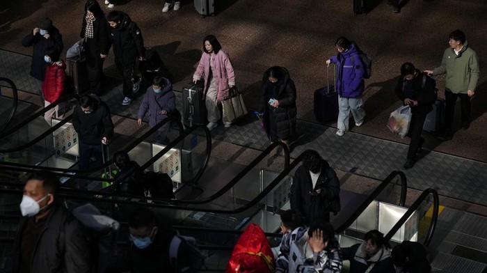 Travelers with their luggage walk beneath a trains departure board at the West Railway Station in Beijing, Saturday, Feb. 3, 2024. Millions of Chinese are expected to travel during the Lunar New Year holiday period this year. (AP Photo/Andy Wong)