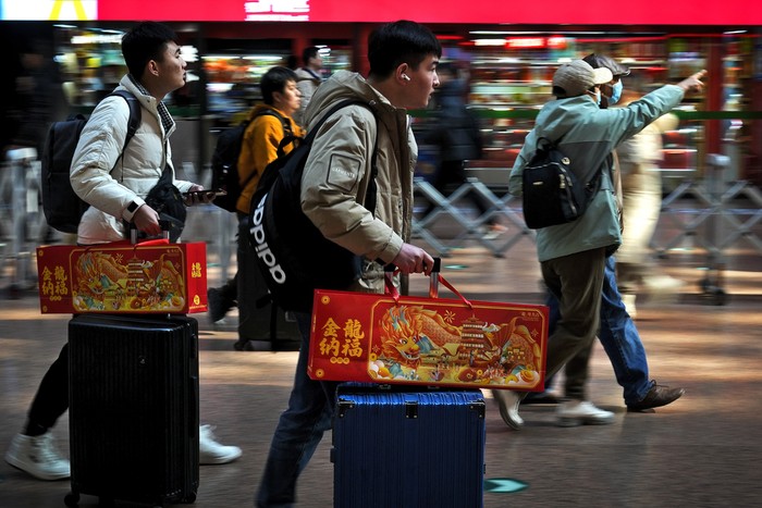 Travelers with their luggage walk beneath a trains departure board at the West Railway Station in Beijing, Saturday, Feb. 3, 2024. Millions of Chinese are expected to travel during the Lunar New Year holiday period this year. (AP Photo/Andy Wong)