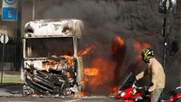 Warga menghentikan sepeda motornya melihat truk yang terbakar di tengah jalan. 