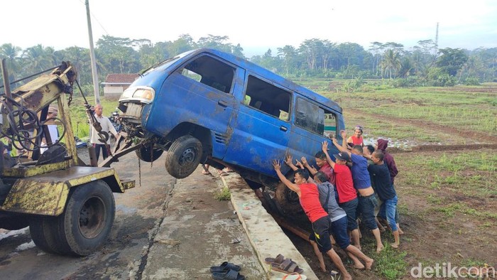 Warga bergotong royong mengangkat mobil angkutan umum yang terguling ke sawah di Pawindan Ciamis.