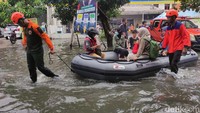 Petugas BPBD Jawa Timur mengearhkan perahu karet saat membantu evakuasi pengendara yang terjebak banjir di Jalan Pepeplegi, Waru.