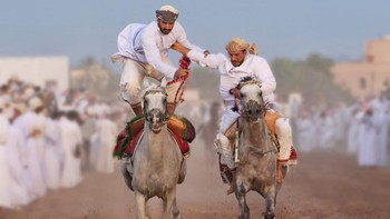 Karya Abdulla AL-Mushaifri dari Qatar. Salah satu pengendara tersebut hendak terjatuh setelah ia mencoba berdiri di atas punggung kudanya, namun rekannya mendukungnya dan memegang tangannya. Foto ini diambil di Kesultanan Oman, di mana pacuan kuda masih diselenggarakan dalam tradisi balap klasik peer-to-peer. Foto: Sony World Photography