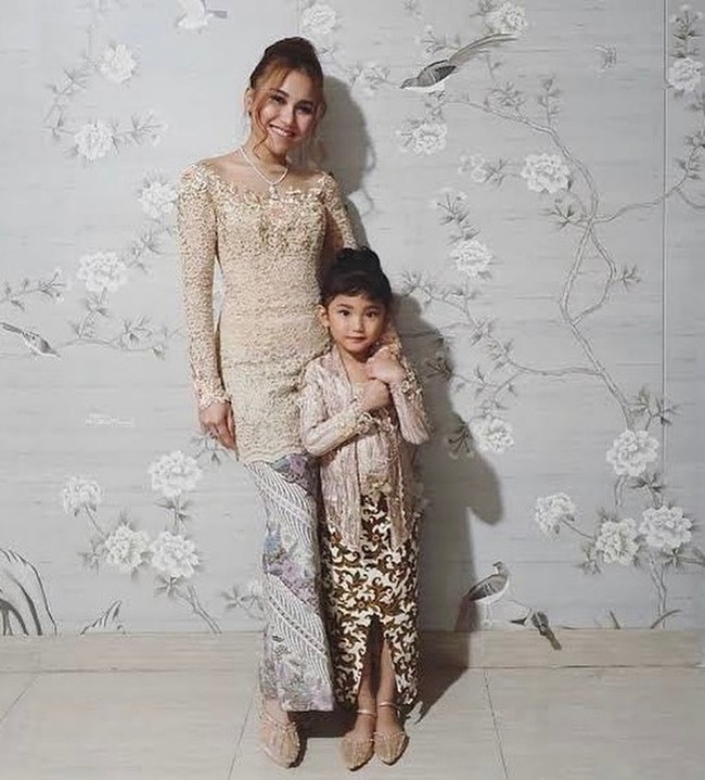 Kebaya kerah sabrina warna earth tone membuat Ayu Ting Ting tampil anggun sekaligus modern. Penyanyi 31 tahun itu memadukan kebayanya dengan kain warna senada dan kembaran dengan putrinya Bilqis. Foto: Dok. Instagram