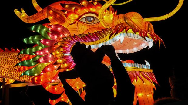 A man and a toddler are silhouetted as they pose for a souvenir photo with a giant dragon lantern decorated near the popular Houhai Lake in Beijing, Thursday, Feb. 8, 2024. Chinese will celebrate Lunar New Year on Feb. 10 this year which marks the Year of the dragon on the Chinese zodiac. (AP Photo/Andy Wong)