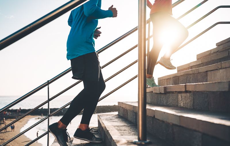 View of runners legs training outdoor - Young couple doing a workout session on stairs next the beach at sunset - Healthy people, jogging and sport lifestyle concept