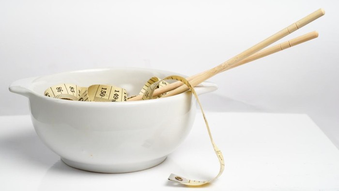 Measuring tape and chopsticks in a white bowl. Weight control concept