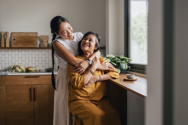 Seorang wanita Asia yang tersenyum menikmati minum teh sementara putrinya yang tercinta memeluknya.