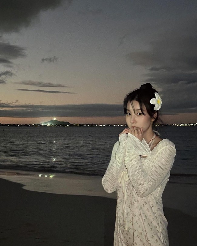 Pelantun ‘Flash’ itu juga pergi ke pantai untuk mengejar sunset. Seperti dalam foto ini, Kwon Eunbi terlihat anggun memakai dress putih. Penampilannya dipermanis dengan aksesori berbentuk bunga kamboja. Foto: dok. Instagram @silver_rain.__