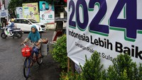 Penjual jamu keliling melintas di dekat alat peraga kampanye di Makassar, Sulawesi Selatan, Senin (12/2/2024).