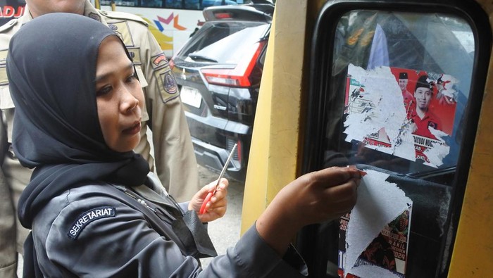 Pengemudi angkutan umum membersihkan stiker alat peraga kampanye (APK) yang terpasang di kendaraannya di Terminal Tawang Alun, Jember, Jawa Timur, Senin (12/2/2024). Petugas gabungan dari Bawaslu, Dinas Perhubungan dan Satpol PP membersihkan APK yang terpasang diangkutan umum dalam masa tenang Pemilu 2024. ANTARA FOTO/Seno/rwa.