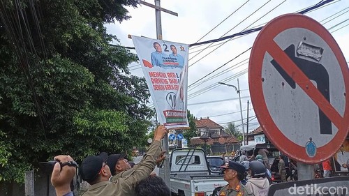 Petugas Satpol PP Badung membersihkan jalan protokol lintas kabupaten di Badung dari semrawutnya APK di masa tenang Pemilu, Senin (13/2/2024). (Agus Eka/detikBali)
