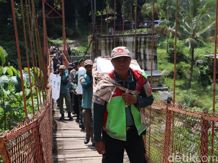 Petugas mendistribusikan logistik pemilu lewat jembatan gantung menuju Grumbul Cibun, Desa Sunyalangu, Kecamatan Karanglewas Kabupaten Banyumas, Selasa (13/2/2024).