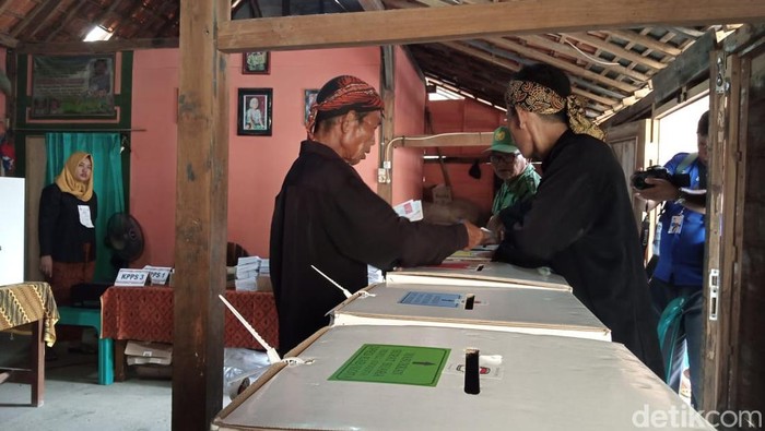 Suasana sedulur sikep di TPS mengenakan baju adat. Mereka tampak memasukkan surat suara ke dalam kotak suara.