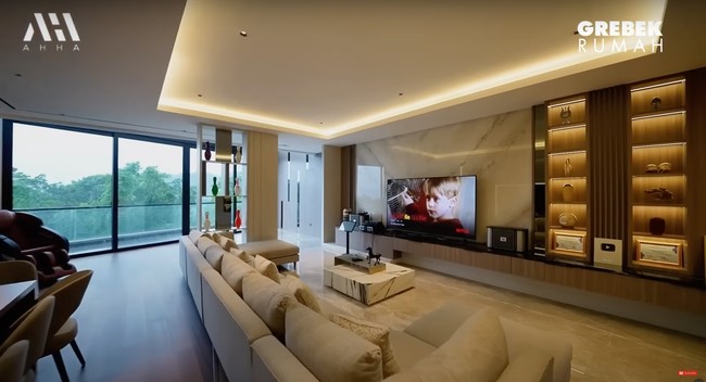 Bagian ruang keluarganya terlihat begitu nyaman dengan dilengkapi sofa dan lantai marmer. Untuk mempercantik ruangan, terdapat beberapa pajangan di lemari sebelah TV. Foto: YouTube/AH