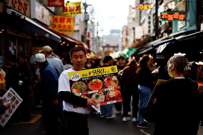 An employee of a seafood restaurant holds a placard displaying the menu to attract customers at Tsukiji Outer Market in Tokyo, Japan February 15, 2024.  REUTERS/Issei Kato