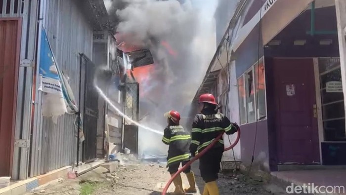 2 petugas damkar tampak menyemprotkan air ke arah bangunan yang terbakar di Kota Padang, Sumatera Barat. (Jeka Kampai/detikSumut)