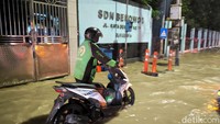 Seorang ojek onlin sedang mendorong motornya yang mogok usai menerjang banjir di kawasan Benowo.