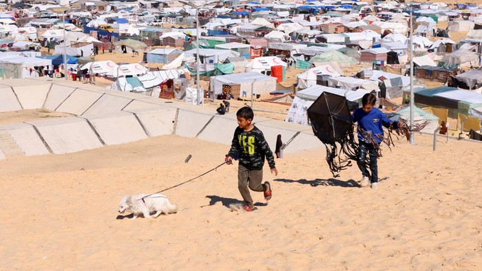 Children walk with a dog, as displaced Palestinians, who fled their houses due to Israeli strikes, take shelter in a tent camp, amid the ongoing conflict between Israel and the Palestinian Islamist group Hamas, at the border with Egypt, in Rafah in the southern Gaza Strip, February 8, 2024. REUTERS/Saleh Salem


     TPX IMAGES OF THE DAY