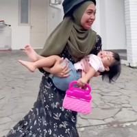 Tak ketinggalan Ria Ricis juga ikutan membuat video parodi aksi Mayor Teddy. Kali ini yang digendong Ricis ialah anaknya sendiri, Moana. Moana yang sedang berdiri membawa tas pink itu tertawa usai tiba-tiba digendong oleh sang bunda. Foto: TikTok