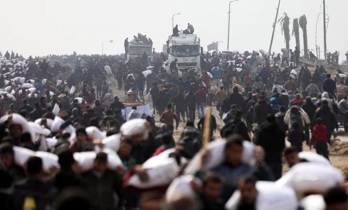 Palestinians carry bags of flour they grabbed from an aid truck near an Israeli checkpoint, as Gaza residents face crisis levels of hunger, amid the ongoing conflict between Israel and Hamas, in Gaza City, February 19, 2024. REUTERS/Kosay Al Nemer/File Photo Purchase Licensing Rights