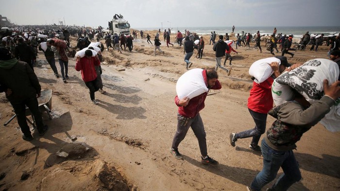 Palestinians carry bags of flour they grabbed from an aid truck near an Israeli checkpoint, as Gaza residents face crisis levels of hunger, amid the ongoing conflict between Israel and Hamas, in Gaza City, February 19, 2024. REUTERS/Kosay Al Nemer