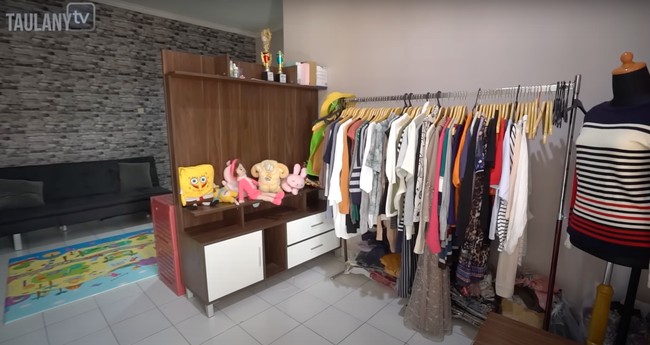 Masuk ke bagian dalam rumah disambut dengan koleksi pakaian milik Dede dan keluarga, serta boneka-boneka sang anak. Pakaian tersebut tampak rapih tergantung, sementara boneka-boneka sang anak berjejer di atas sebuah lemari kayu. Foto: YouTube/Taulany TV