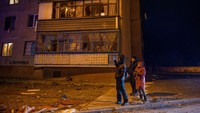 Orang-orang berdiri di depan gedung apartemen yang rusak di seberang stasiun pemurni air yang terkena serangan rudal Rusia.