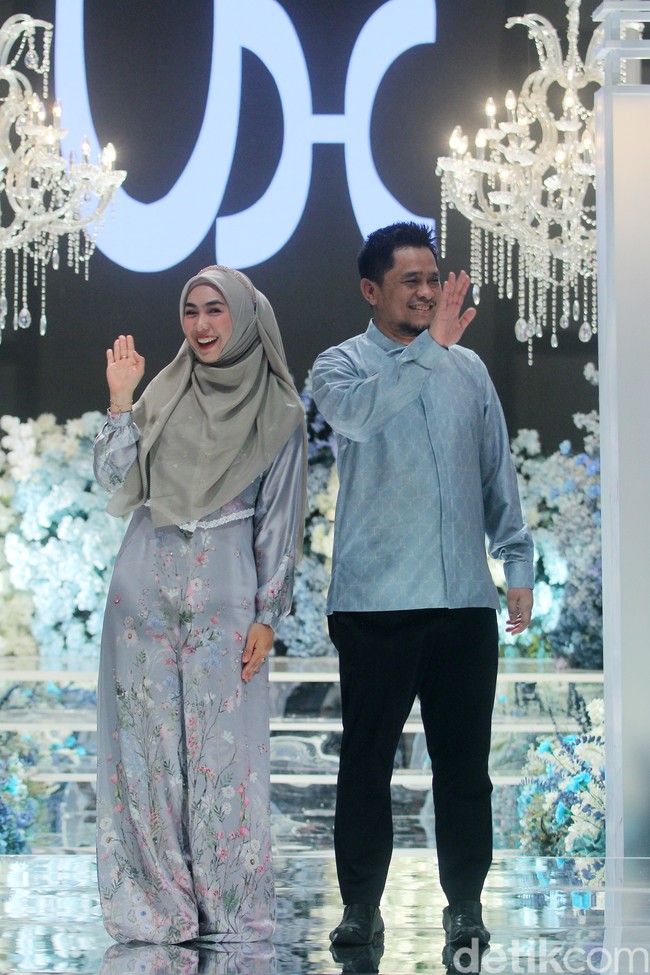 Oki Setiana Dewi bersama suami, Ory Vitrio membawakan koleksi baju Lebaran sarimbit 2024. Oki memakai hijab pashmina syari dipadu dengan dres silk. Sedangkan Ori tampil dengan baju koko bahan silk dan celana hita Foto: Mohammad Abduh/detikcom.