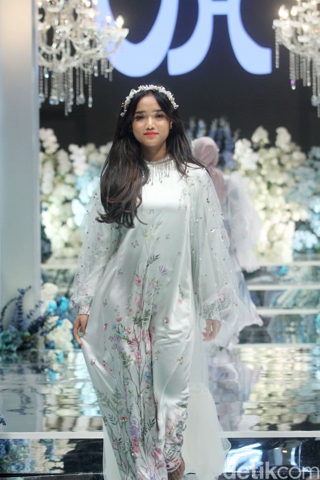 Fujianti Utami Putri memakai dress silk putih dipadu dengan long outer lace, dilengkapi dengan bando dengan detail beads yang membuat semakin feminin. Fuji pun tampil percaya diri dan menebar senyuman saat berlenggok di cat walk. Foto: Mohammad Abduh/detikcom.