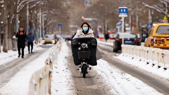 A woman rides a scooter on a road following snowfall in Beijing, China February, 21, 2024. REUTERS/Tingshu Wang Purchase Licensing Rights
