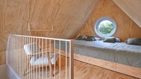 Sementara itu, bagian kamar tidurnya berada seperti di atas loteng dengan jendela bulat. Kasur yang disediakan cukup besar yang bisa memuat 4 orang. Foto: Jeroen Musch via Dezeen