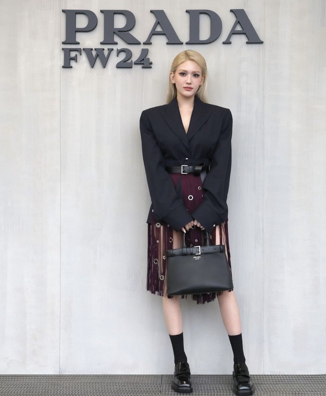 Jeon Somi yang viral disebut ‘Barbie hidup’ dengan rambut pirang dan wajah blasteran, mewakili Prada. Dia mengenakan setelan jas hitam dan rok berwarna burgundy dengan aksen rumbai-rumbai, yang mempertegas pinggang semutnya. Foto: Instagram