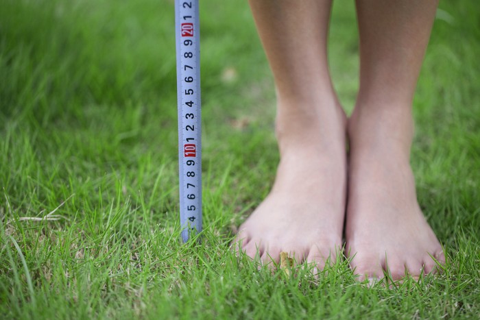 Close-up of persons feet measuring height with measurement tape.