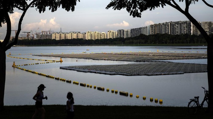 Joggers pass by a floating solar panel farm on the Bedok Reservoir lined by apartment buildings in Singapore, Sunday, July 16, 2023. In 2006 the government launched the Active, Beautiful, Clean Waters Program which transformed the country's water systems into more public areas for the public to enjoy. Through the program, reservoirs are now areas where residents can kayak, hike and picnic, giving a greater sense of ownership and value to the country's water supplies. (AP Photo/David Goldman)