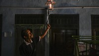 Seorang peternak menyalakan lampu yang menggunakan energi dari limbah kotoran sapi.   