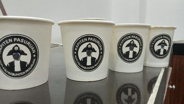Wajah Gus Irsyad di logo Kapiten Pasuruan pada cup kopi dicoreti.