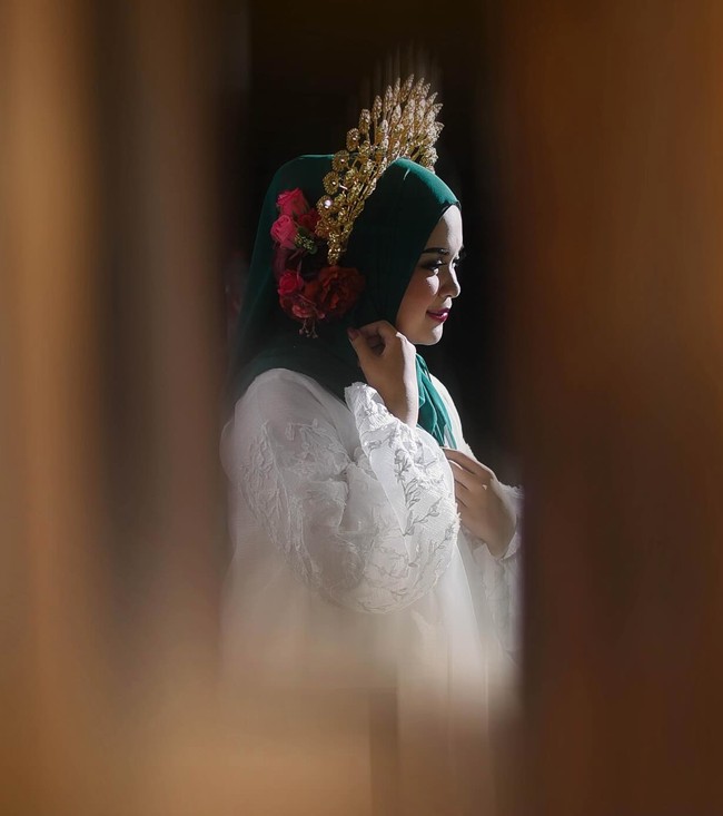 Tampil cantik menjadi pengantin Bugis, Ihsani Nurul Izzah tampak melengkapi penampilannya dengan aksesori kepala yang menyerupai mahkota, yang biasa disebut Saloko Pinang Goyang. Ia kemudian mempercantiknya dengan menambahkan beberapa tangkai bunga mawar merah paada bagian samping. Foto: Instagram/@andiamarms