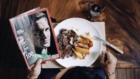 Begini potret estetik Angga saat makan dan baca majalah. Ia menikmati steak dengan kentang panggang yang terlihat menarik selera. Foto: Instagram anggapuradiredja