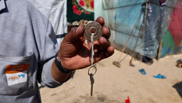 Kunci, Kenangan Terakhir Rumah Warga Gaza Hussein Abu Amsha, a displaced Palestinian man whose house was destroyed by Israeli strikes amid the ongoing conflict between Israel and Hamas, holds up the key of his destroyed house with an ancient Palestinian coin, outside his tent in Rafah, in the southern Gaza Strip, February 26, 2024. REUTERS/Ibraheem Abu Mustafa
