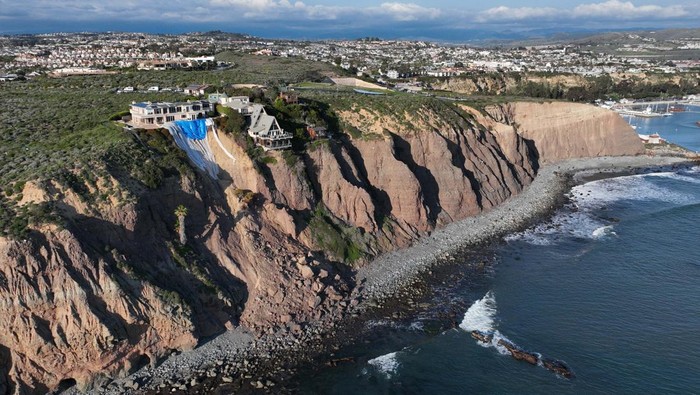 Dana Point, CA - February 27: An aerial view of a double A-frame cliff-side mansion, between two other mansions affected by a landslide and protective tarps to protect from further slides from upcoming storms in Dana Point Tuesday, Feb. 27, 2024. The three homes affected by recent rain storms are being monitored but officials say they don't appear to be in imminent danger. (Allen J. Schaben / Los Angeles Times via Getty Images)