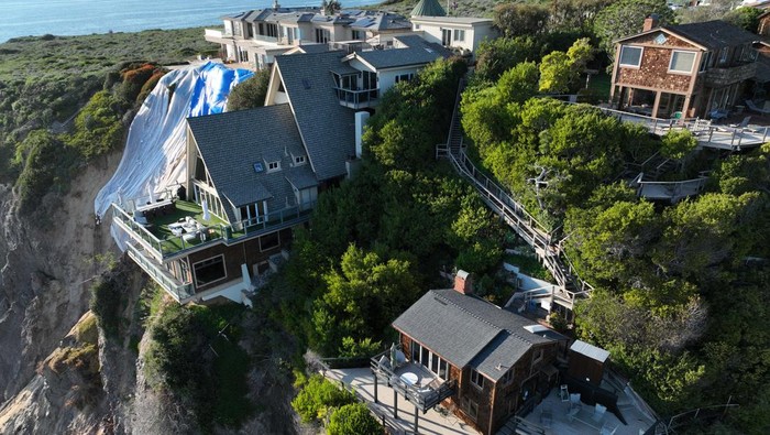Rumah Terancam Longsor di Tebing Dana Point, California Dana Point, CA - February 27: An aerial view of a double A-frame cliff-side mansion, between two other mansions affected by a landslide and protective tarps to protect from further slides from upcoming storms in Dana Point Tuesday, Feb. 27, 2024. The three homes affected by recent rain storms are being monitored but officials say they don't appear to be in imminent danger. (Allen J. Schaben / Los Angeles Times via Getty Images)