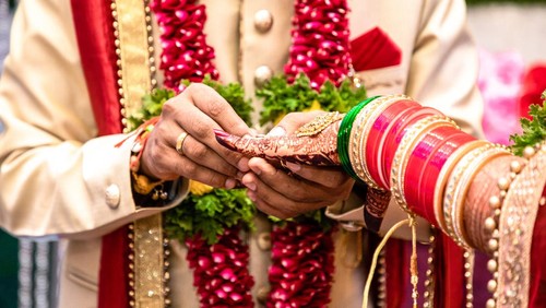 Beautiful photo of a ring ceremony being held as per Hindu rituals. Bridegroom is putting a ring to her Bride. Both dressed in traditional hindu marriage attire.