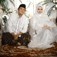 Wanita asal Madiun ini memilih gaun putih dengan aksen kristal, bordir dan payet yang dipadankan jilbab putih. Senada dengan sang istri, Denny Caknan memakai baju koko berhias bordiran yang dipadankan kain batik dan peci. Foto: Instagram/@denny_caknan @bellabonita_r.a