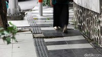 Seorang sedang melintasi pedestrian di Jalan Darmo dengan kondisi keramik mulai rusak.